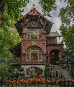 an old victorian style house in the middle of trees and flowers on the front lawn