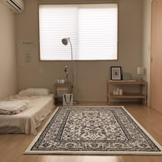 a bedroom with a bed and rug in the floor next to a window that has blind shades on it