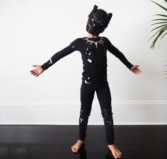 a young boy wearing a cat mask and black wetsuit standing in front of a white wall