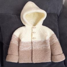 a crocheted sweater with a hood and buttons on the front is sitting on a couch