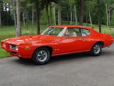 an orange muscle car is parked on the side of the road in front of some trees