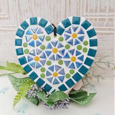 a heart shaped ceramic decoration sitting on top of a white table next to green leaves