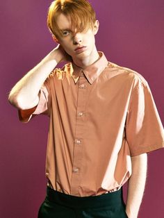 a man with red hair wearing a brown shirt and black pants, standing in front of a purple background