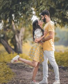 a man and woman standing next to each other on a dirt road with trees in the background