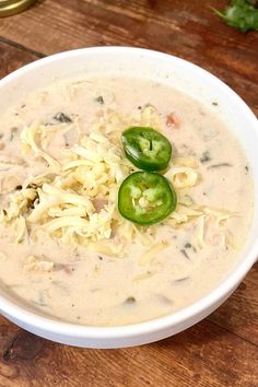 a white bowl filled with pasta and green peppers on top of a wooden table next to a can