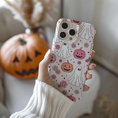 a woman holding up her phone case with ghost and pumpkins all over the back