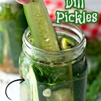 a person is holding a pickle in a mason jar filled with cucumbers