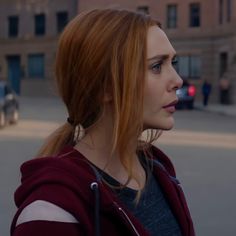 a woman with red hair is standing in the middle of an empty street and looking off into the distance