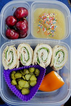 a plastic container filled with lots of food next to grapes and apples on top of a blue table cloth