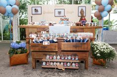 a wooden table topped with lots of boxes filled with cake and candy covered in blue balloons