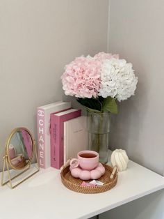 pink and white flowers are in a vase next to a cup on a small table