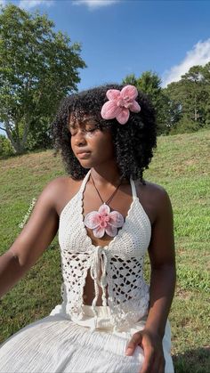 a woman sitting in the grass wearing a white dress with pink flowers on her head