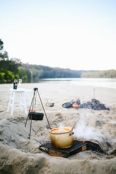 there is a pot on top of a stove in the sand near a fire pit