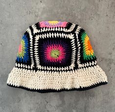 a multicolored crocheted hat laying on top of a cement floor next to a wall