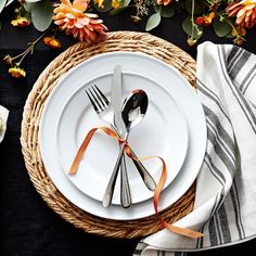 the table is set with white plates, silverware and orange flowers on black linens