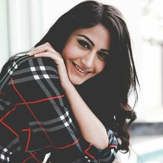 a woman posing with her hand on her shoulder and smiling at the camera while wearing a plaid shirt