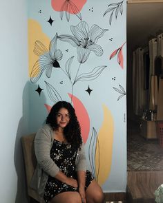 a woman sitting on a chair in front of a wall with flowers painted on it