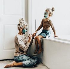 a woman and child with face paint sitting on the edge of a bathtub in front of a door