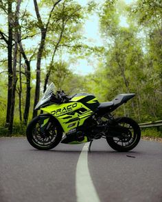 a yellow and black motorcycle parked on the side of a road in front of trees