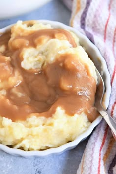 a bowl filled with mashed potatoes covered in gravy on top of a table