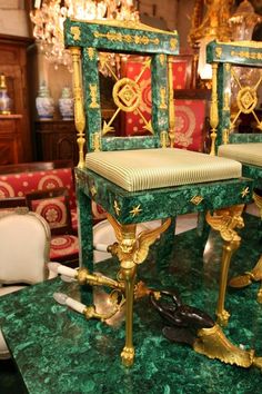 two green and gold chairs sitting on top of a marble table next to each other