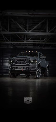 a large black truck parked in a garage next to a metal structure with lights on