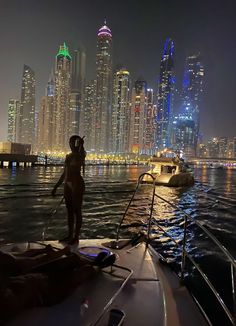 a woman standing on the bow of a boat in front of a city at night