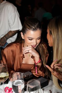 two beautiful young women sitting at a table with wine glasses and plates in front of them