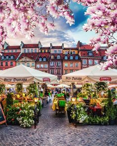 an open air market with tables and umbrellas in front of some buildings on a cobblestone street