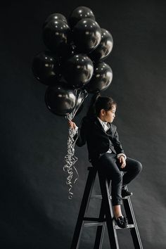 a woman sitting on top of a ladder holding balloons