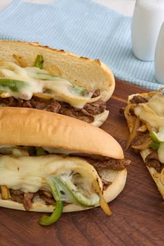 two sandwiches with cheese, meat and onions on a cutting board next to a glass of milk