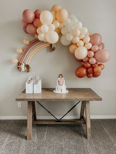 a table topped with balloons and cake next to a rainbow shaped wall hanging on the wall