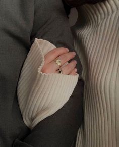 a close up of a person's hand with a ring on their finger, wearing a sweater