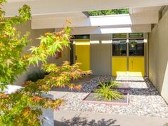 the entrance to a modern home with yellow doors and graveled walkway leading up to it