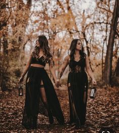 two women holding hands and walking through the woods in black outfits with long sheer skirts