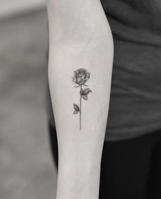 a black and white photo of a single rose tattoo on the left inner arm,