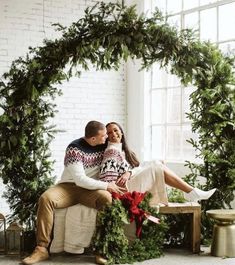 a man and woman sitting on a bench in front of a christmas wreath with greenery