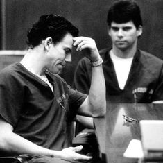 black and white photograph of two men sitting at a table with their hands on their head