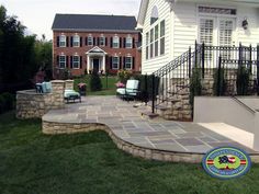 a brick walkway leading to a house with chairs on the lawn and steps up to it