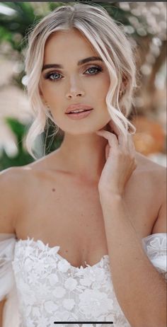 a woman with blonde hair and blue eyes wearing a white wedding dress is looking at the camera