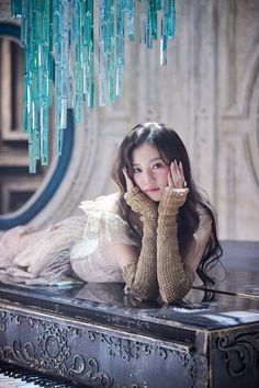 a woman laying on top of a piano under a chandelier