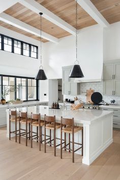 a large kitchen with white cabinets and wooden floors, along with an island that has four stools