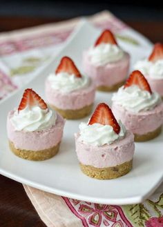 mini strawberry cheesecakes on a white plate with whipped cream and fresh strawberries