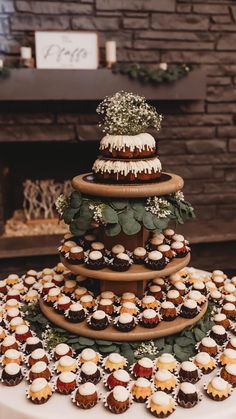 a three tiered cake with cupcakes and greenery on the top is surrounded by other desserts