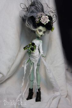 a doll is dressed in white and green with flowers on her head, sitting against a white background