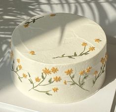 a white cake with yellow flowers painted on it's side sitting on a table