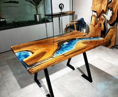 a table made out of wood and glass with blue paint on the top, sitting in front of a window