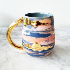 a blue and gold coffee mug sitting on top of a marble counter with golden handles