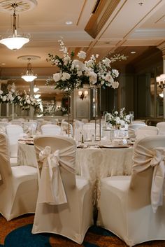 the chairs are covered in white cloths with bows and flower centerpieces on them