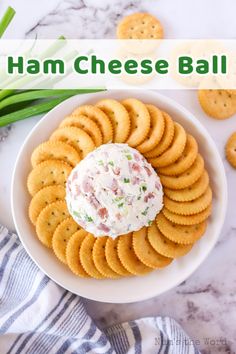 a bowl filled with crackers and cheese ball on top of a white plate next to green onions